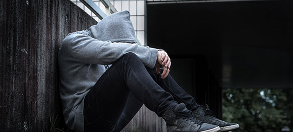 Person sitting gainst a wall alone with head down in arms. Depression, mental illness, suicide, healing.