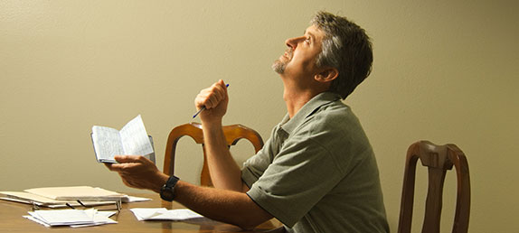 A man covering his face to avoid seeing his credit card praying for his finances and prosperity.