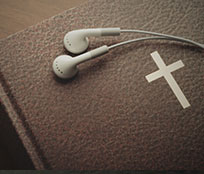 A copy of a black Bible with gold lettering and a pair of white ear buds to listen to the Bible.